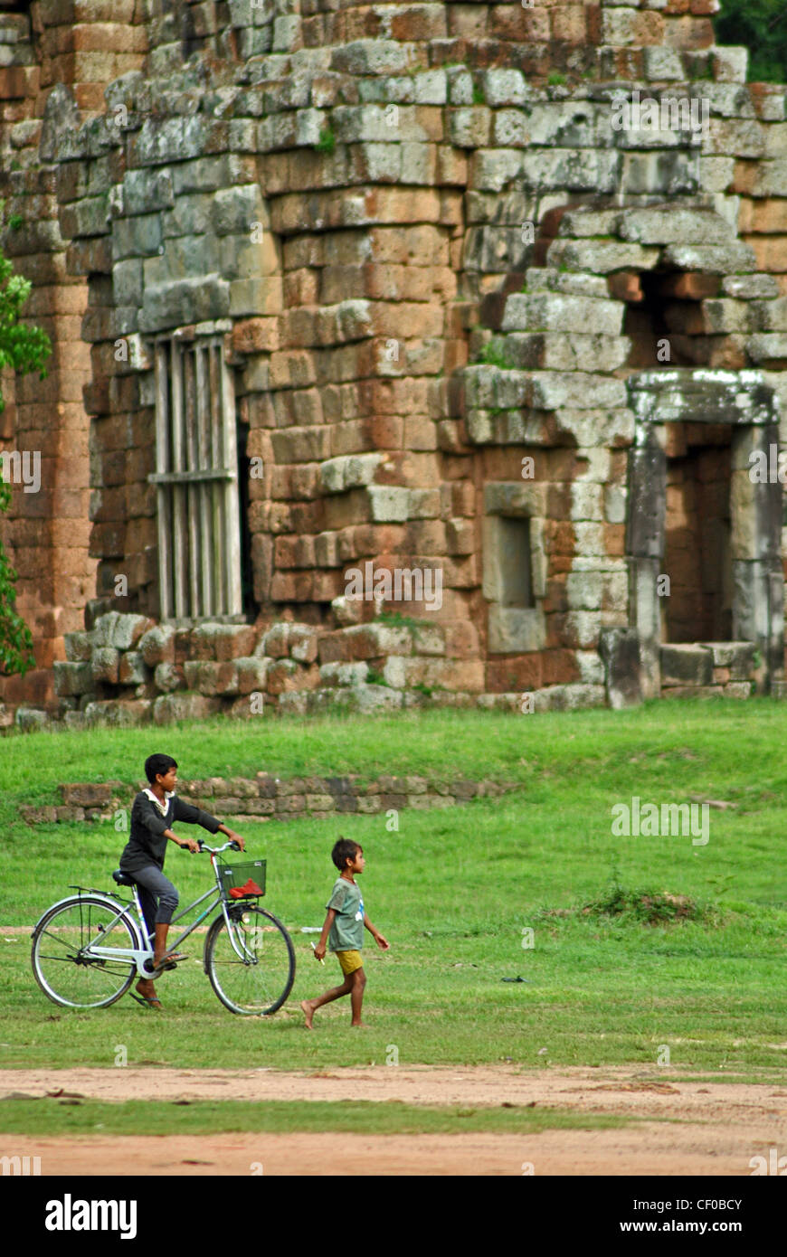 Children cycling past Bayon Thom temple in Siem Reap, Cambodia Stock Photo