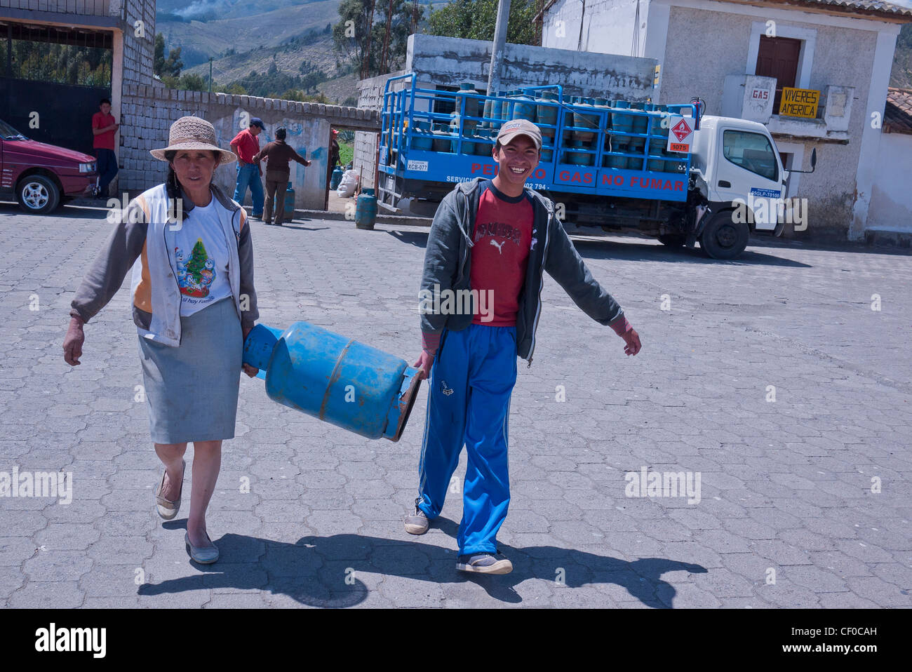A mother and her teenage son carry a propane gas tank across the plaza