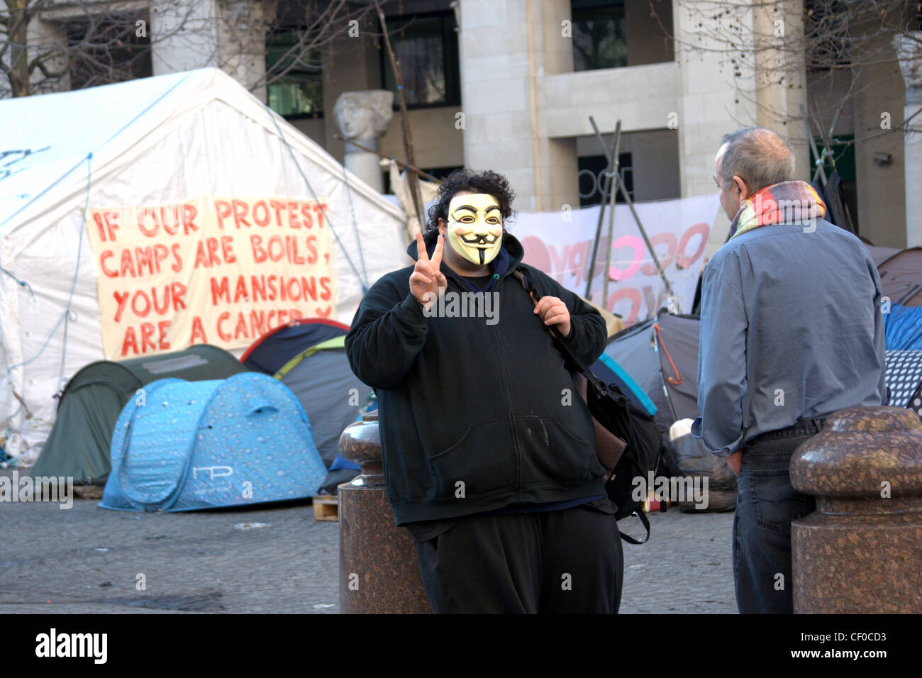 A masked member of Anonymous, part of the peaceful Occupy London protest, in front of tents outside St Paul's Cathedral. Stock Photo