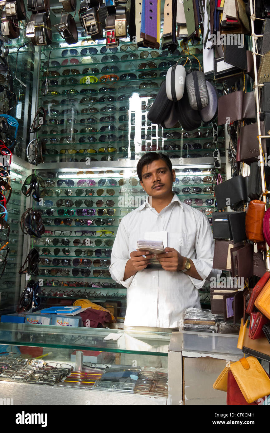 small shop with a young single shopkeeper selling belts and glasses on the streets of Mumbai, Maharashtra, India Stock Photo