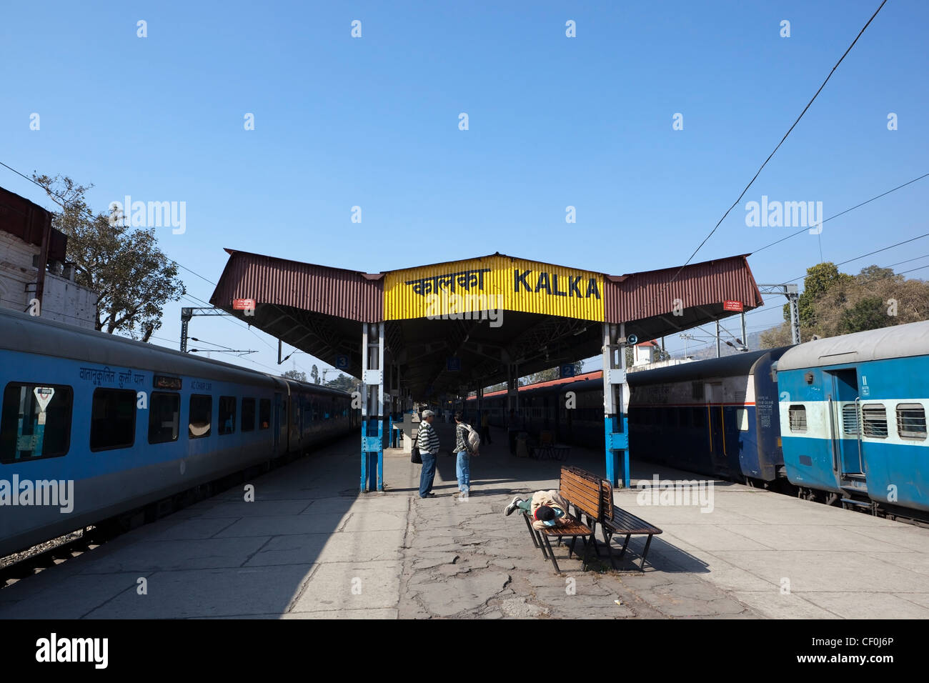 man resting on a bench and people talking as they wait on the platform at kalka railway station in the Haryana, India Stock Photo