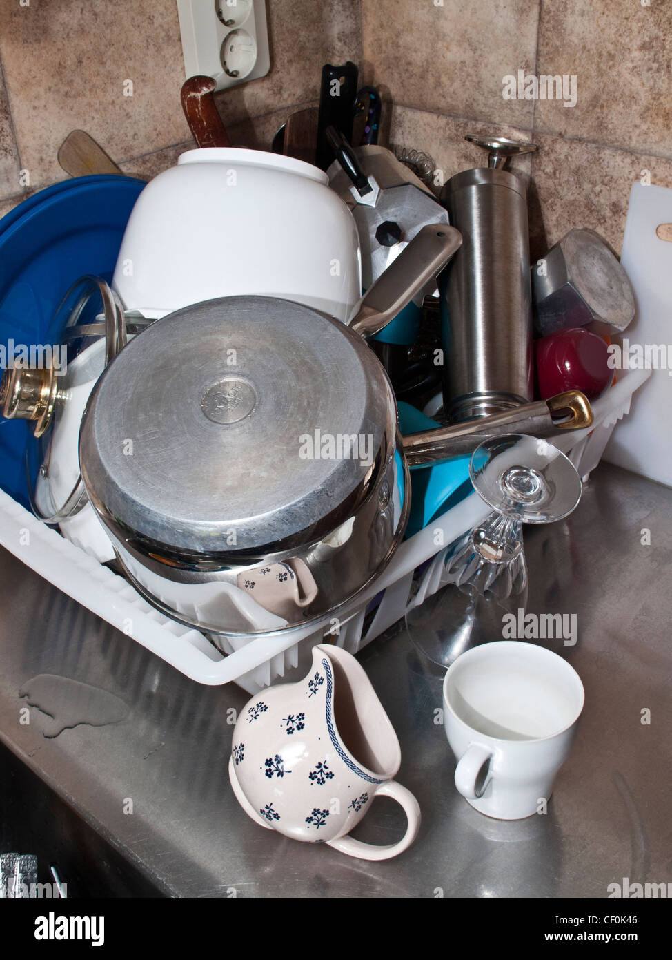 Plastic kitchen drain dish rack full with untidy dishes and utensils ...