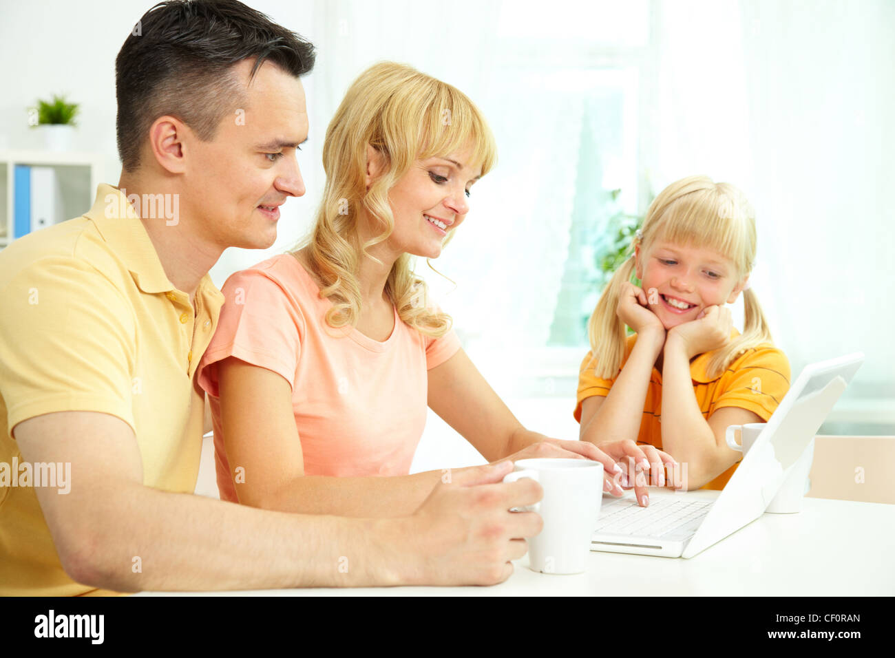 Cheerful family of three using laptop and smiling Stock Photo