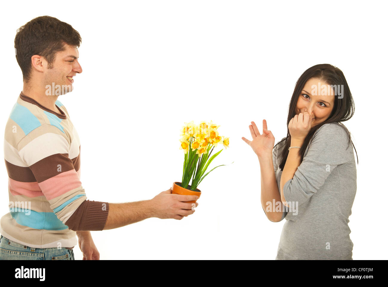 Guy offering daffodil flower to a picky woman who making faces and pinching her nose to avoid the odor of flower isolated Stock Photo