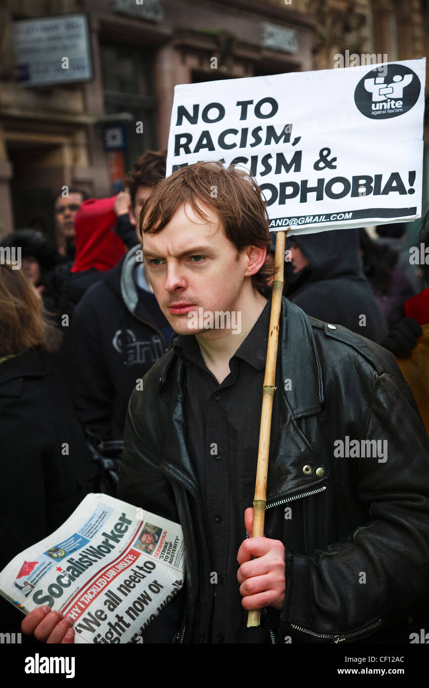 Young man carrying an anti-racism banner and selling 'the Socialist Worker' while at a street demonstration, Glasgow Stock Photo