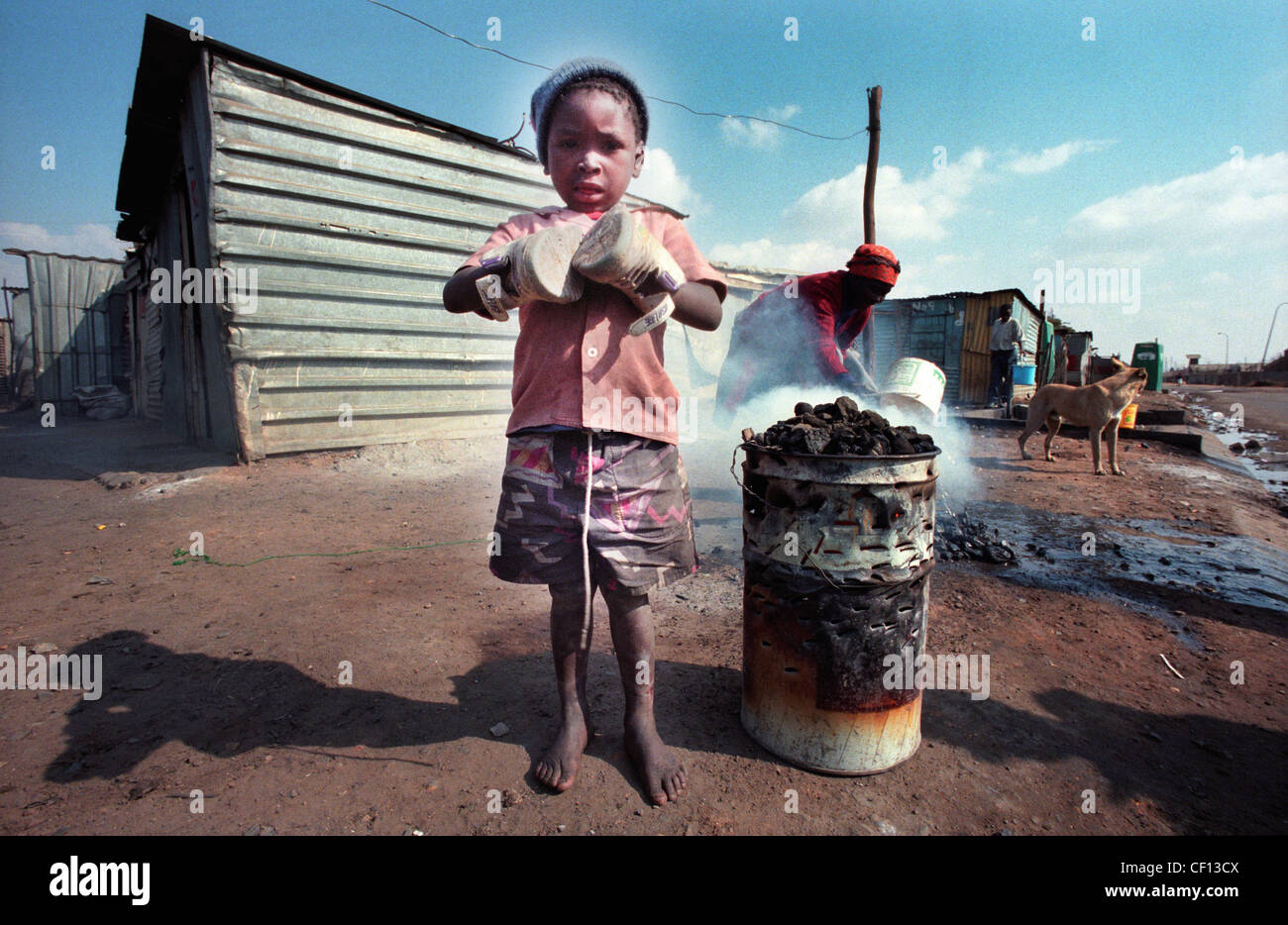 Barefoot Township kid in Soweto, South Africa uses shoes to keep his hands warm Stock Photo