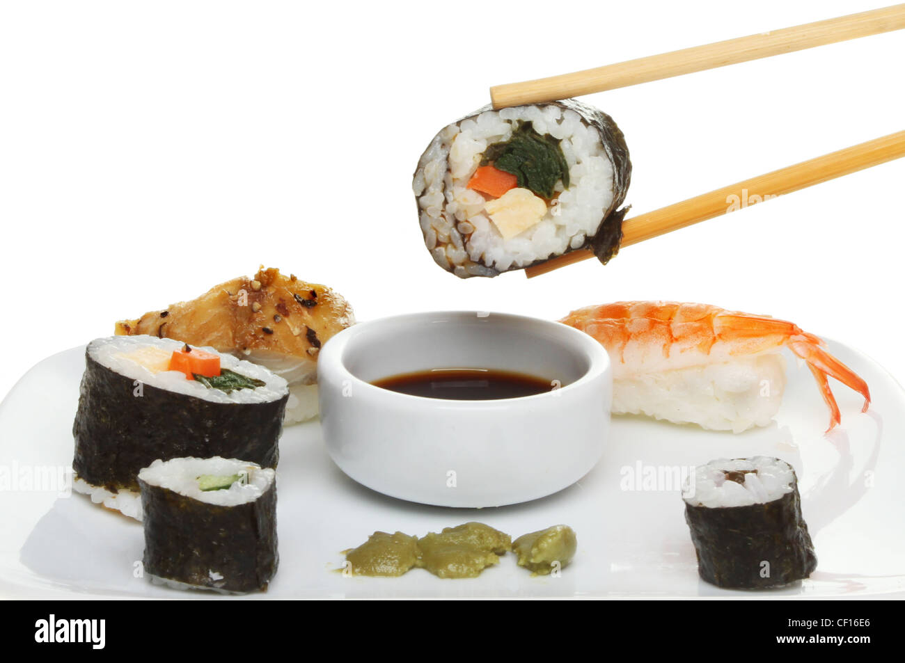 Closeup of sushi on a plate with a piece of makizushi in chopsticks dipped in soy sauce Stock Photo