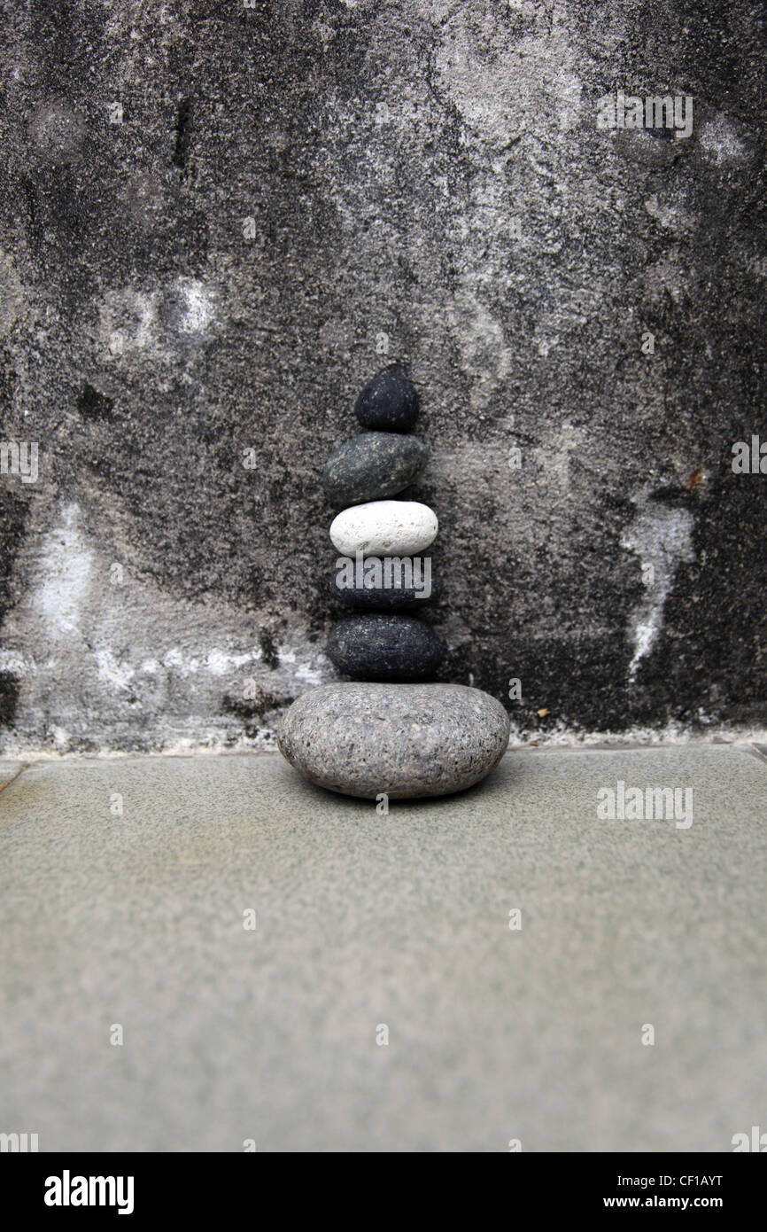 6 stones stands on each others in balance. It's a Zen visual on a rough concrete wall Stock Photo