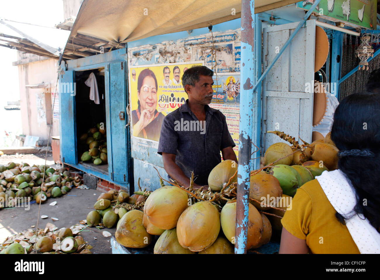a street vendor selling tender coconuts at kanyakumari, india. In the backdrop is a political graffiti. Stock Photo