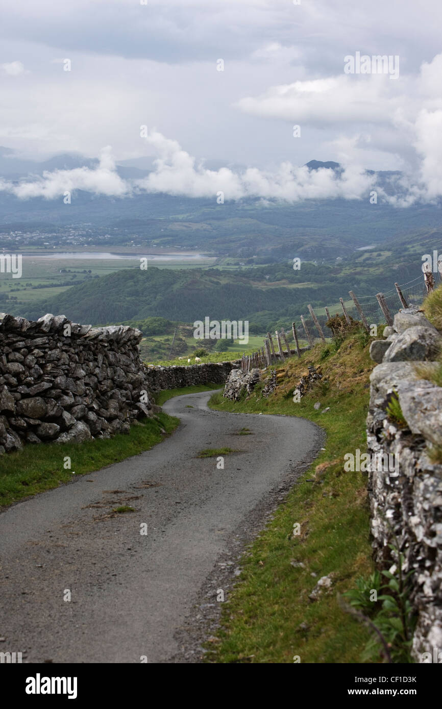 Single track road winding downhill between traditional stone walls in the Snowdonia National Park. Stock Photo