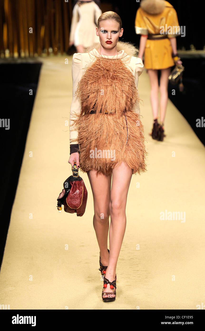 Model wearing a short tan ostrich feather dress long cream sleeves and black tasseled belt, platform sandals red beads, Stock Photo