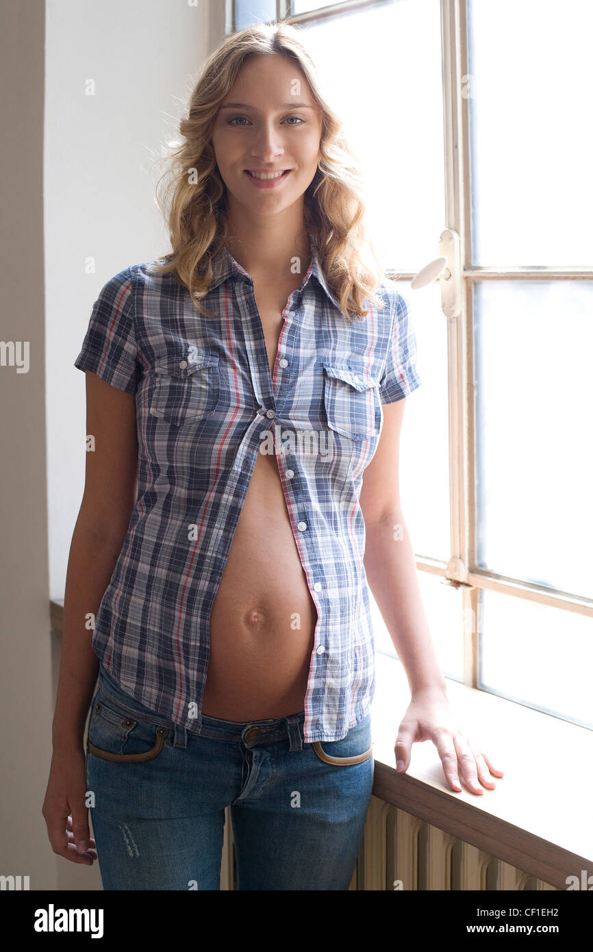 A pregnant female wearing blue denim jeans a blue and red checked short  sleeve shirt only one button done up, exposing her Stock Photo - Alamy