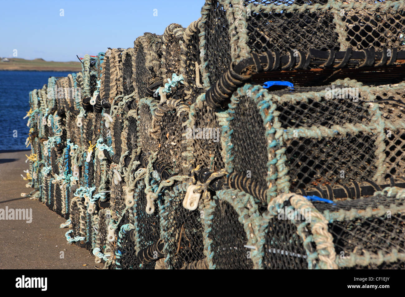 Neatly stacked fishing creels on the slipway in Fionnphort, Isle of Mull with the Isle of Iona in the background Stock Photo