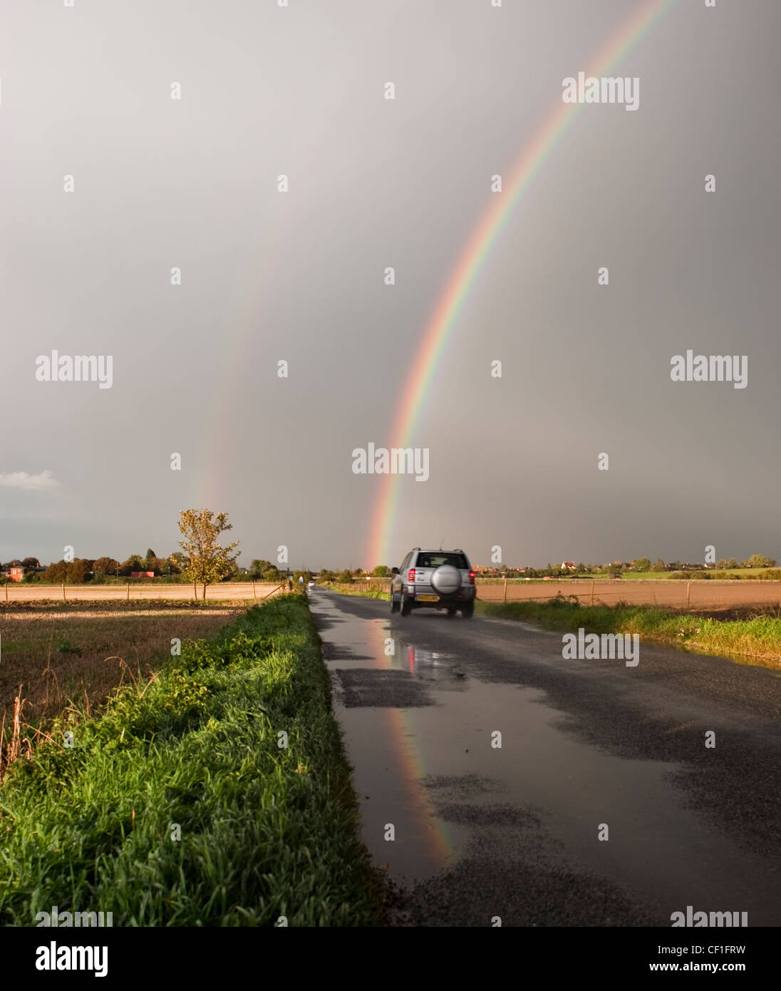 Car driving down road with double rainbow Stock Photo