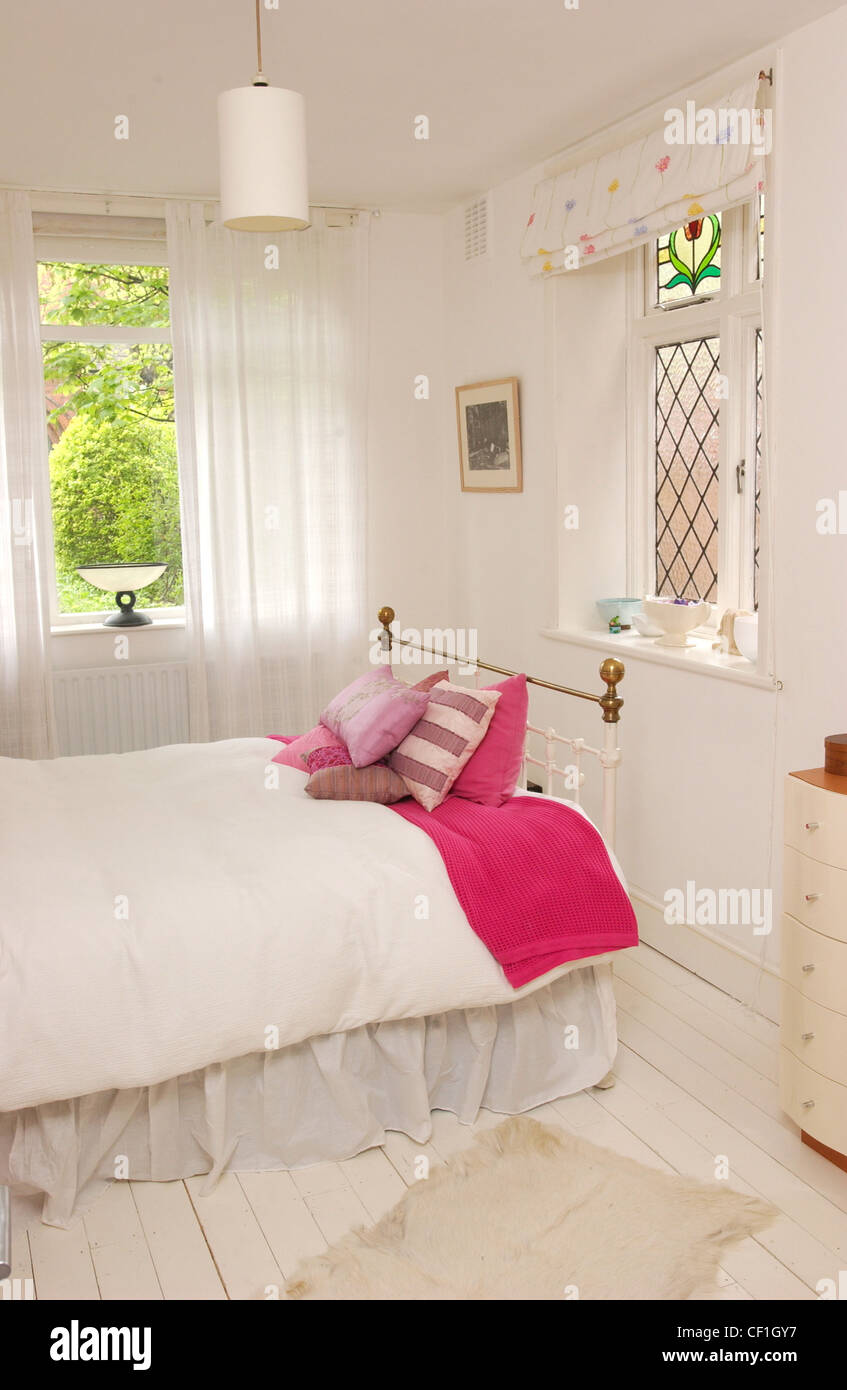 Renovated Flat Interiimage of bedroom iron bed pink cushions, pink throw and white bed linen, white painted floboards, stained Stock Photo