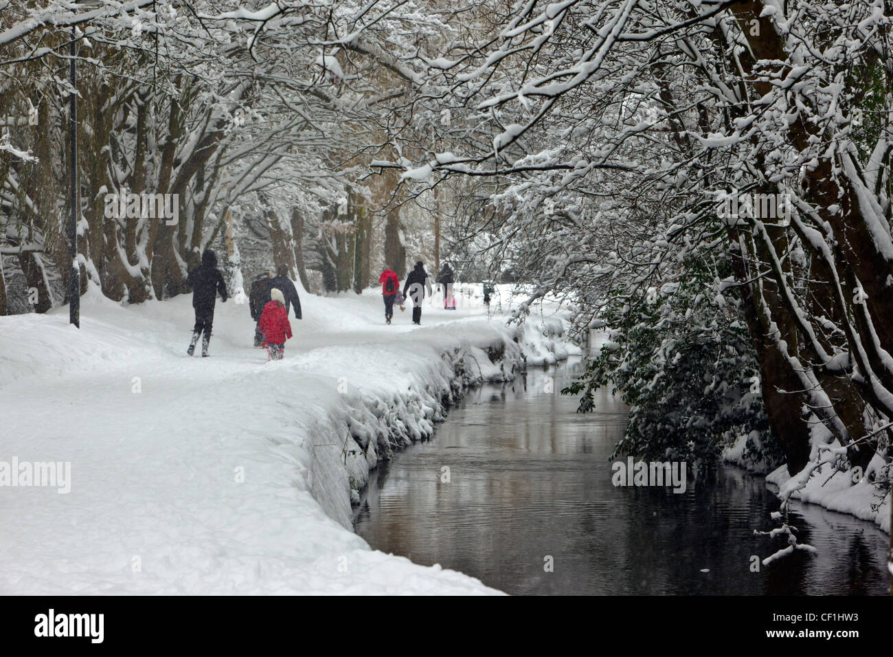 People walking through thick snow along Bow Wow, a lane running alongside the River Churn in winter. Stock Photo