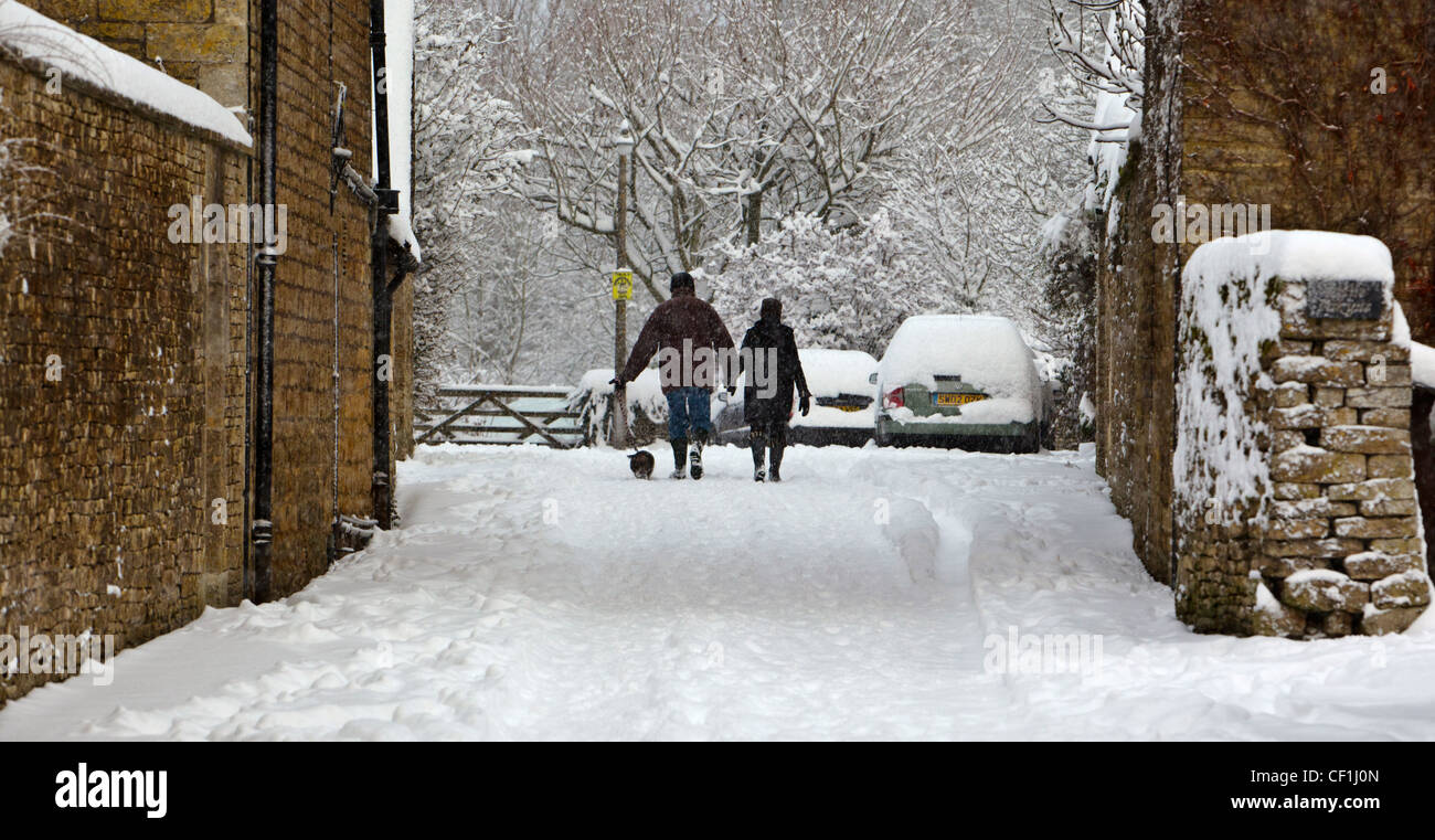 A couple walking a small dog through heavy snow in a Cotswold village. Stock Photo