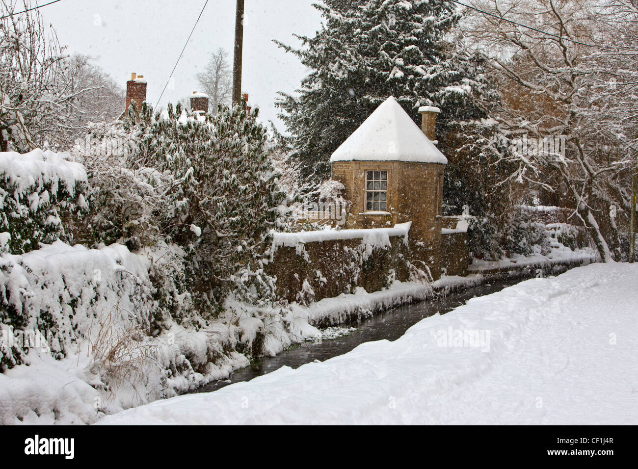 Thick snow covering the oddly named 'Bow Wow', a lane in the Cotswold village of South Cerney running between the River Churn an Stock Photo