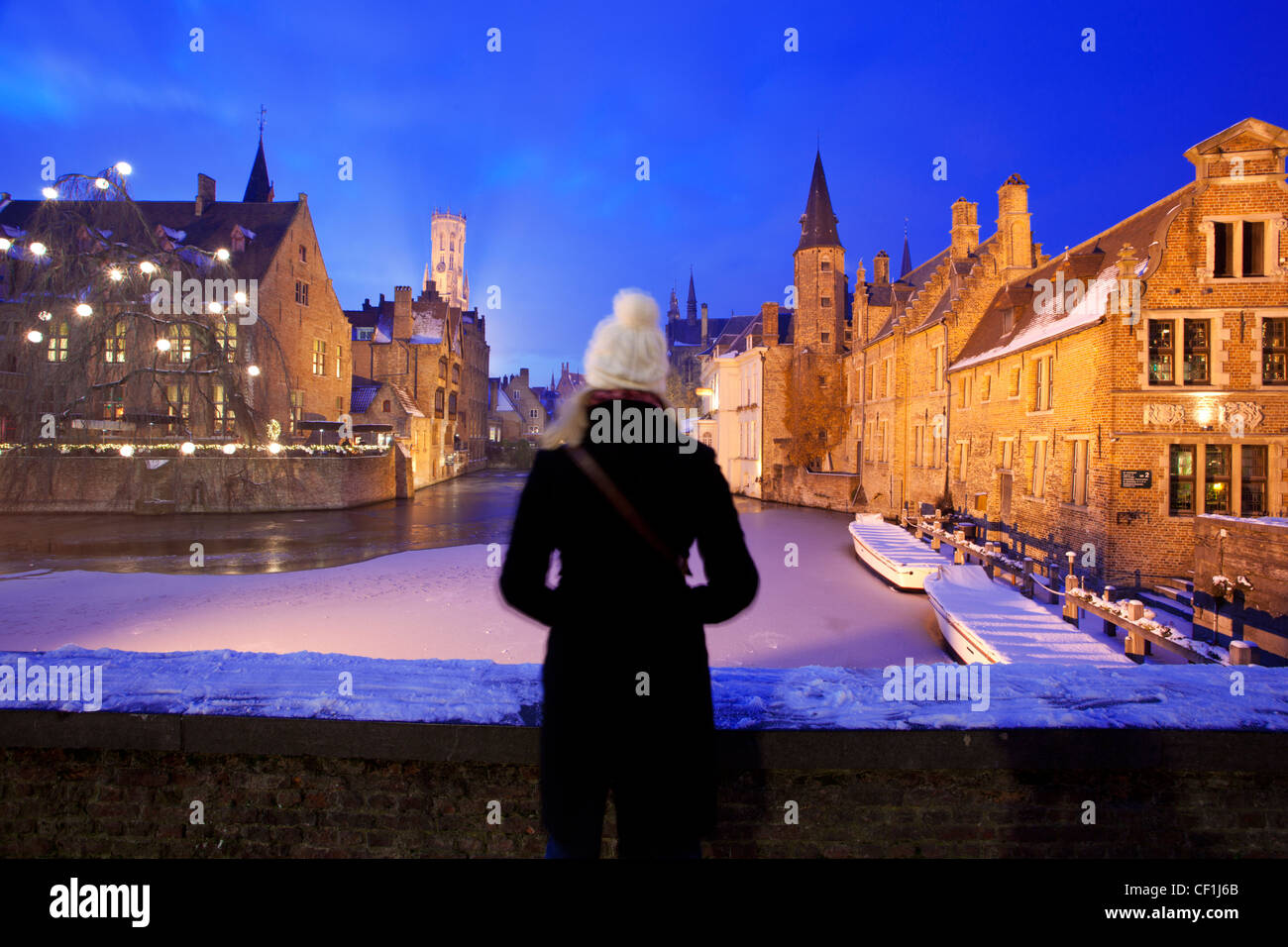 A lady in a warm coat and white bobble hat looks over A view of Rozenhoedkaai with a frozen canal and snow Stock Photo