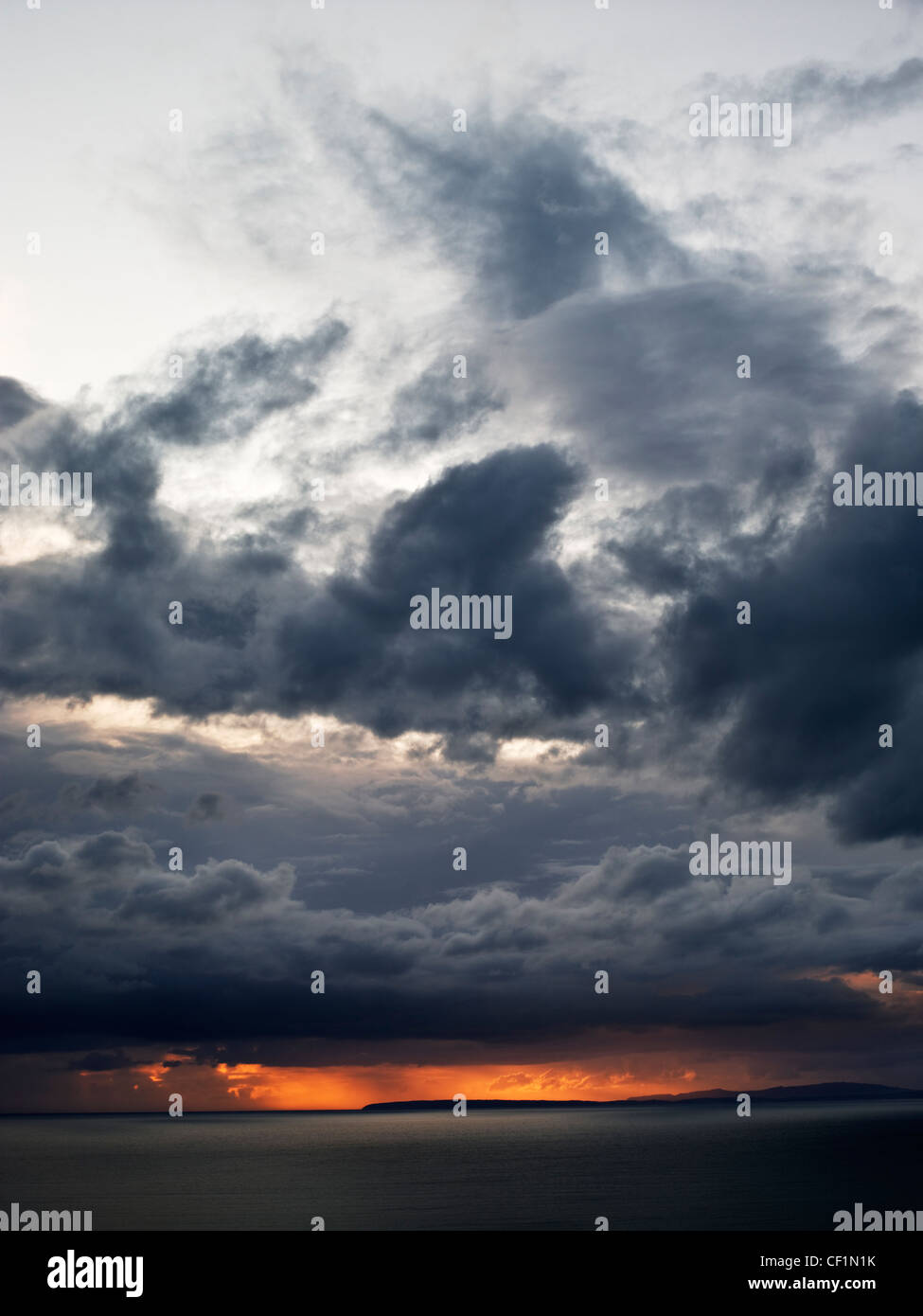 Orange light breaking through storm clouds over the Irish Sea from Llanfair. Stock Photo