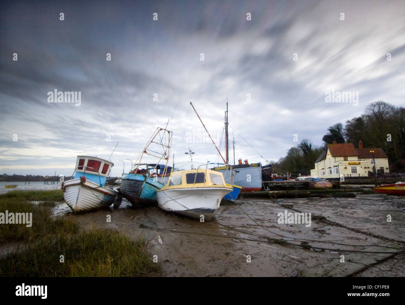 Boats at low tide at Pin Mill. The 17th century Butt & Oyster inn is so close to the river that it can serve pints of ale throug Stock Photo