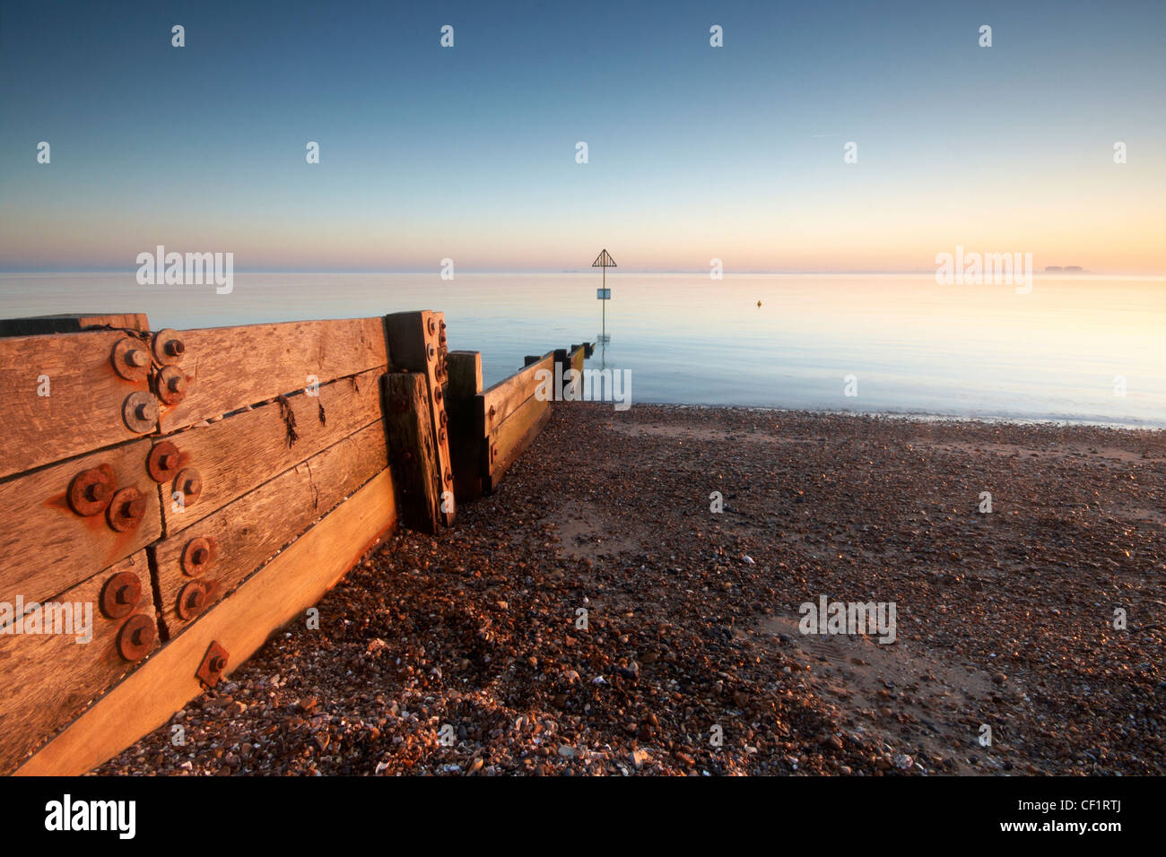 A groyne leading from the beach into tranquil waters at West Mersea in the Thames Estuary at sunset. Stock Photo