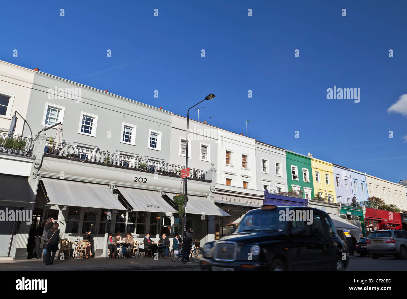 A black London taxi cab passing a row of shops and restaurants in Westbourne Grove. Stock Photo