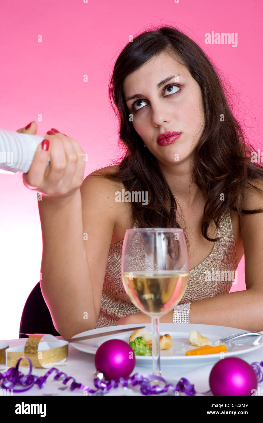 Female long brunette hair diamante hairclip wearing gold halterneck top sitting at table in front of plate small pieces of Stock Photo