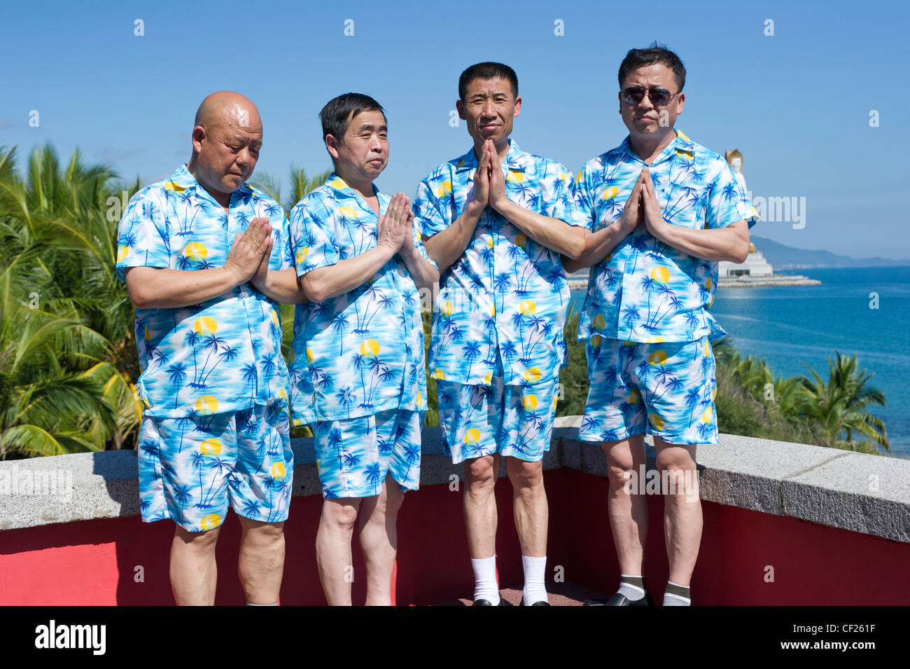 Four Chinese men in matching blue shirts and shorts get their picture taken in a prayer pose Stock Photo