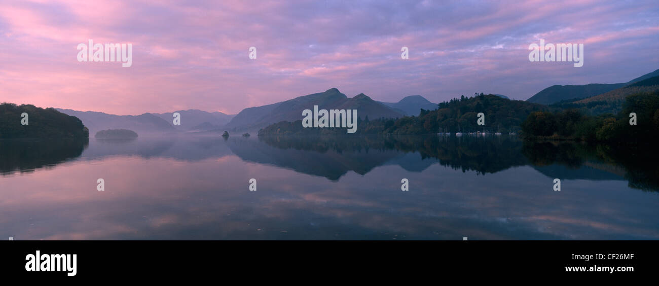 The pastel colours of dawn reflected in the still waters of Derwent Water. Stock Photo