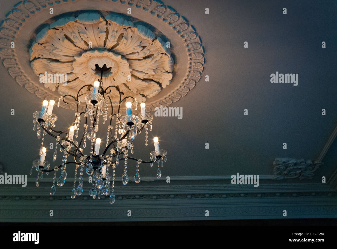 A chandelier hanging from the ceiling surrounded by a detailed plaster surround Stock Photo