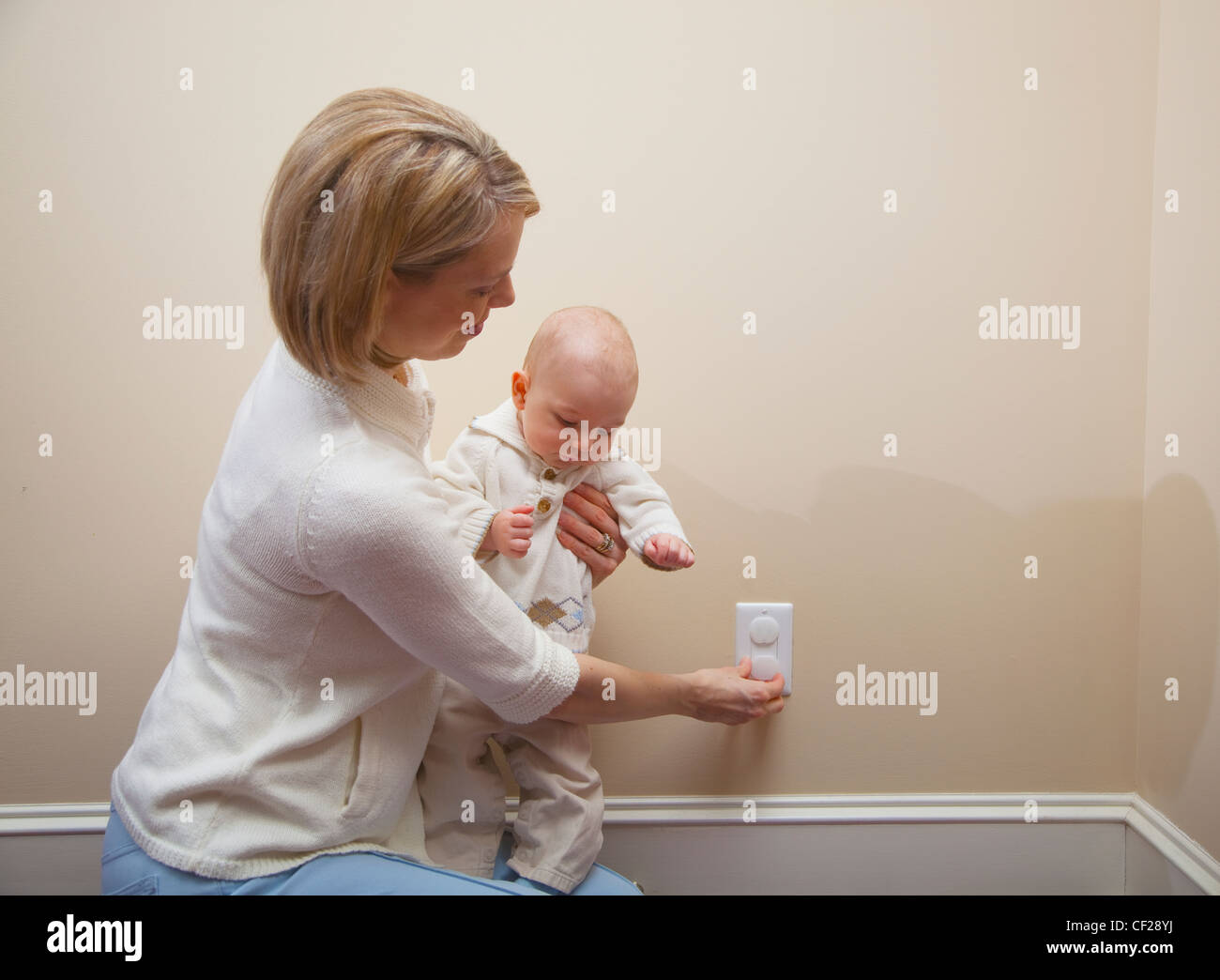 Mother With Baby Applying Safety Plug In Outlet; Jordan Ontario Canada Stock Photo