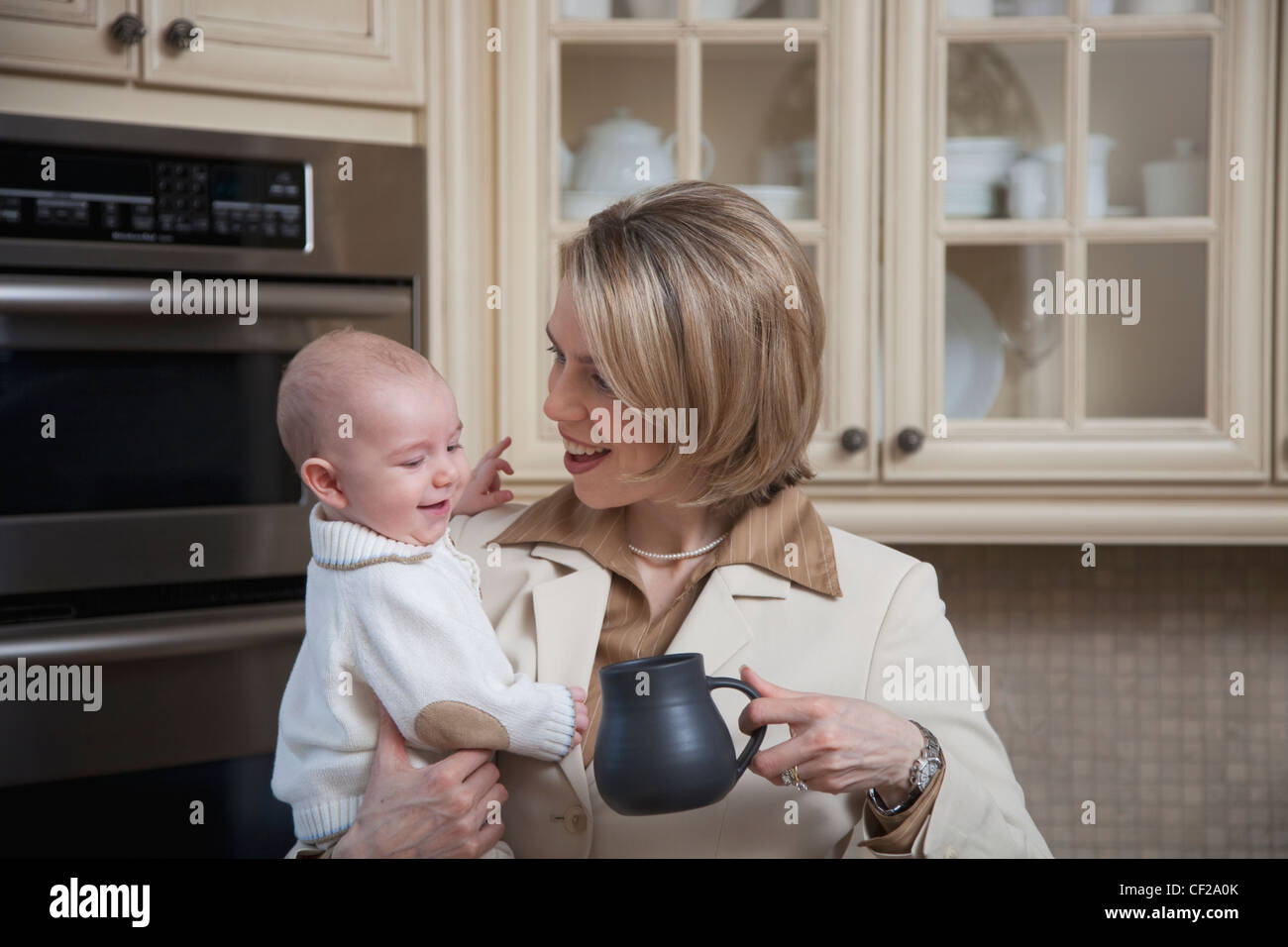 A Businesswoman Holding Her Baby In The Kitchen At Home; Jordan Ontario Canada Stock Photo