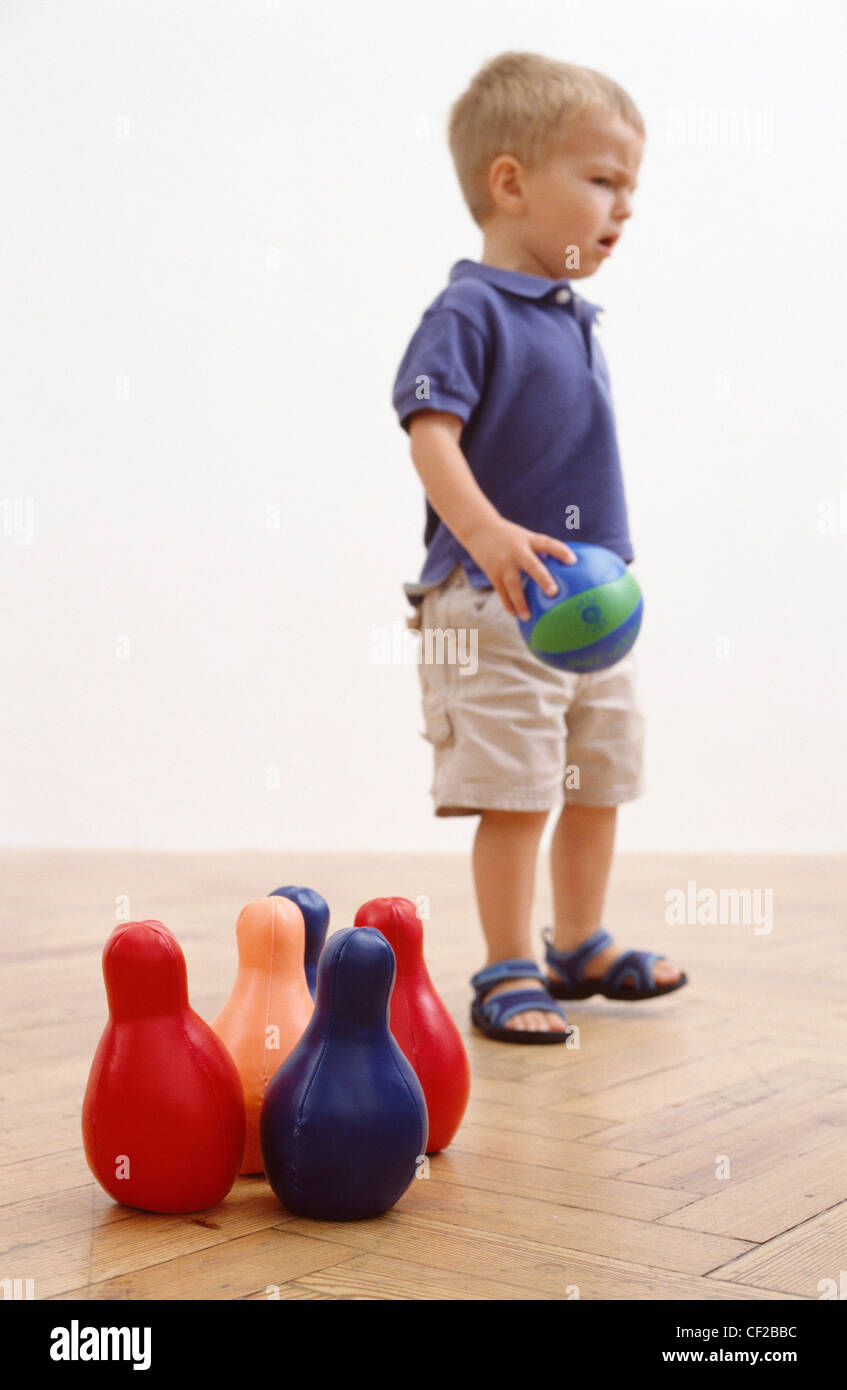 Male toddler with blonde hair wearing a blue t shirt, cream shorts and sandals, playing skittles Ian Boddy Stock Photo