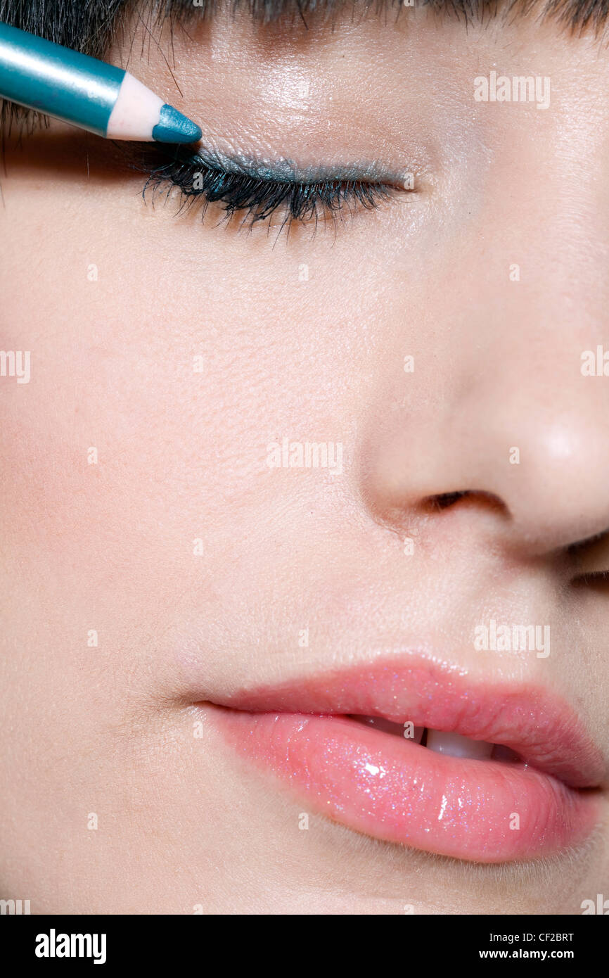 Female applying blue metallic eyeliner to the upper eyelids, unsmiling