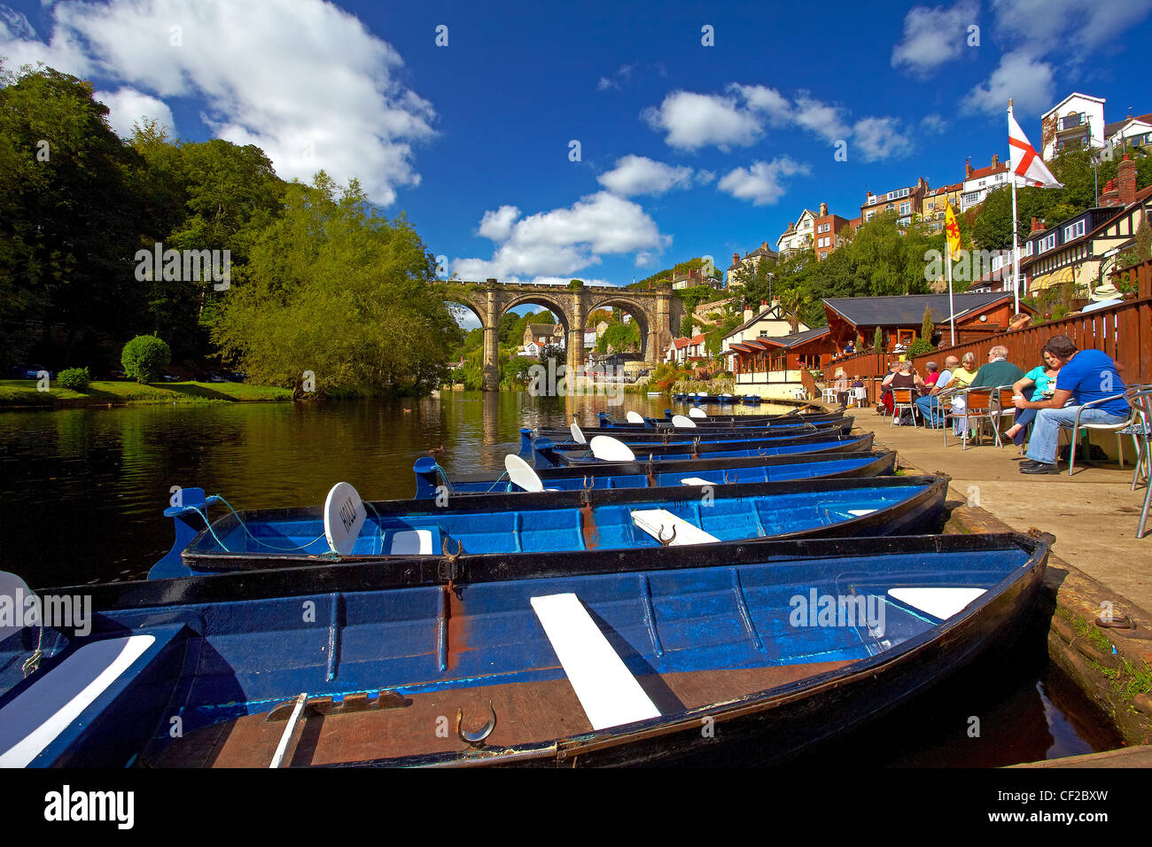Rowing boats for hire and people enjoying a drink at a cafe on the riverside of the River Nidd at Knaresborough. Stock Photo