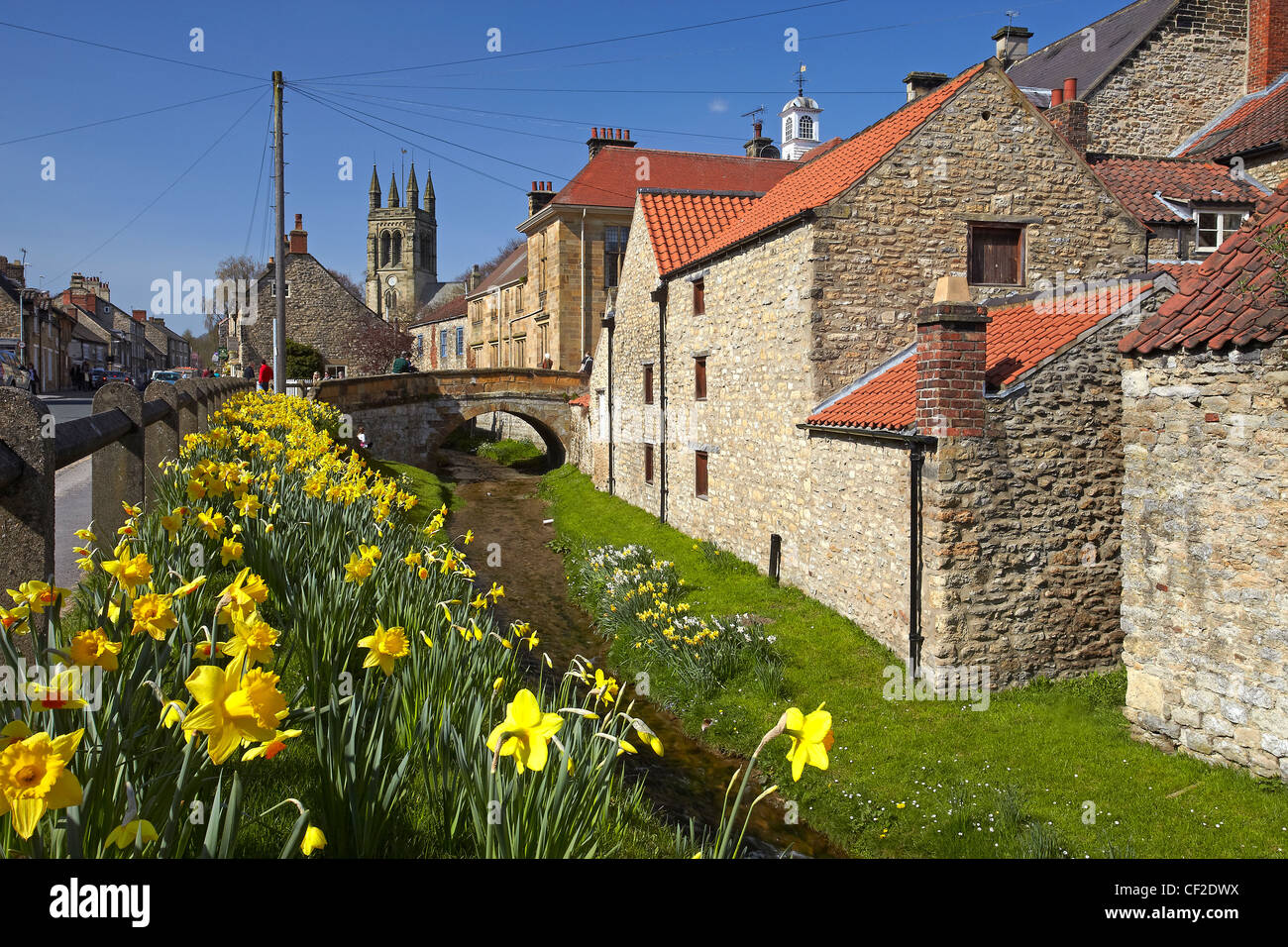 Town Hall, All Saints Church tower and stone bridge over stream lined with daffodils in the village of Helmsley on the edge of N Stock Photo