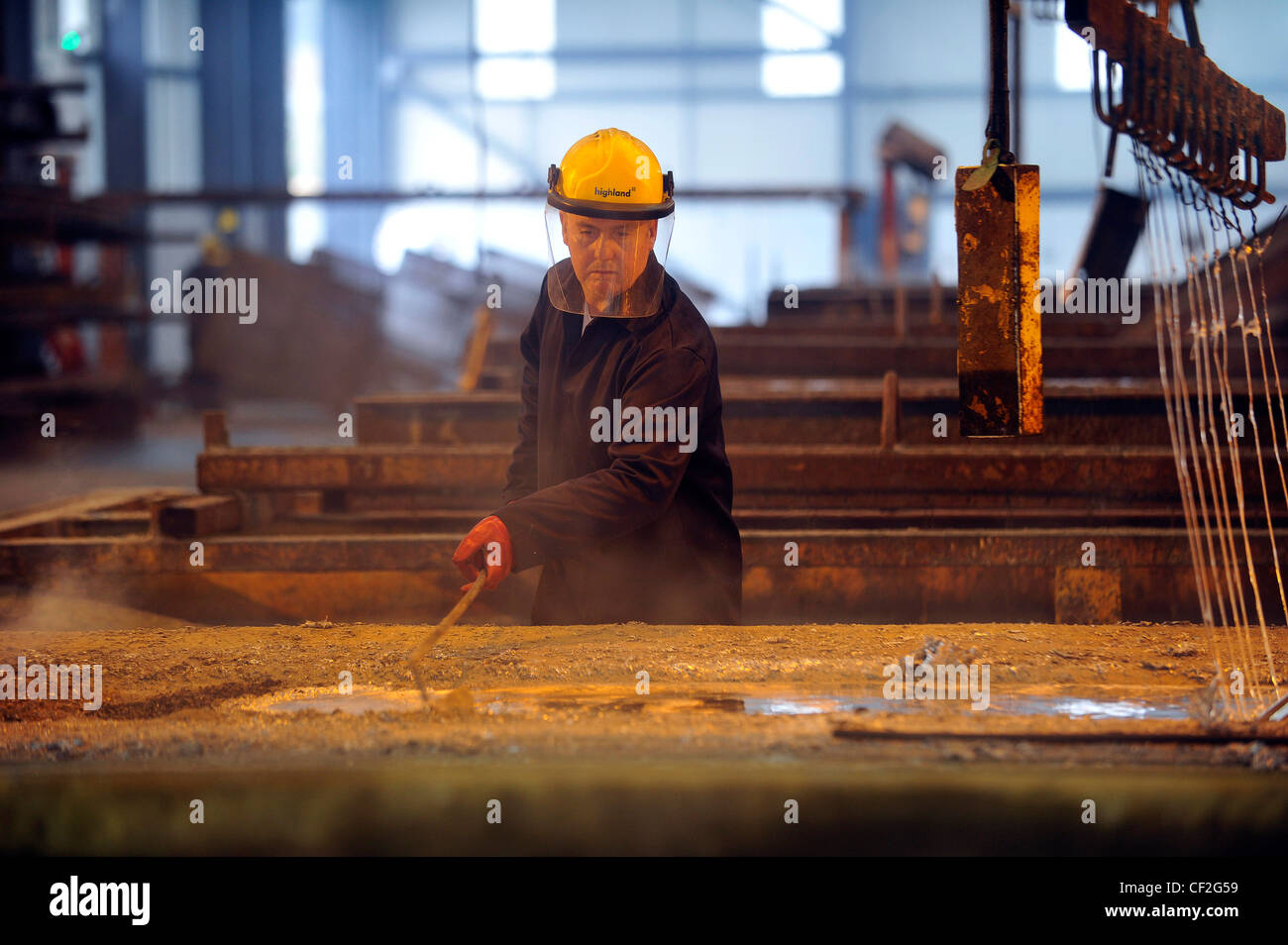 A worker prepares steel and skims molten zinc at a galvanizing plant