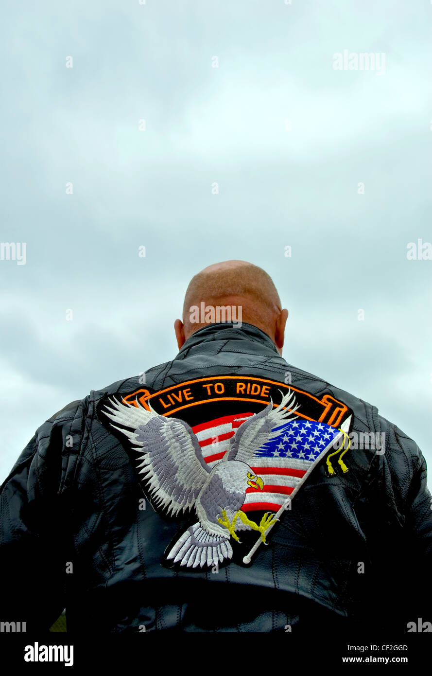 A biker wearing a leather jacket with an eagle carrying a stars and stripes flag emblem on the back. Stock Photo