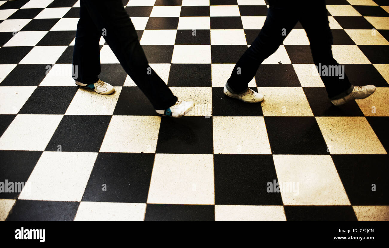 Two people walking across a black and white chequered floor. Stock Photo