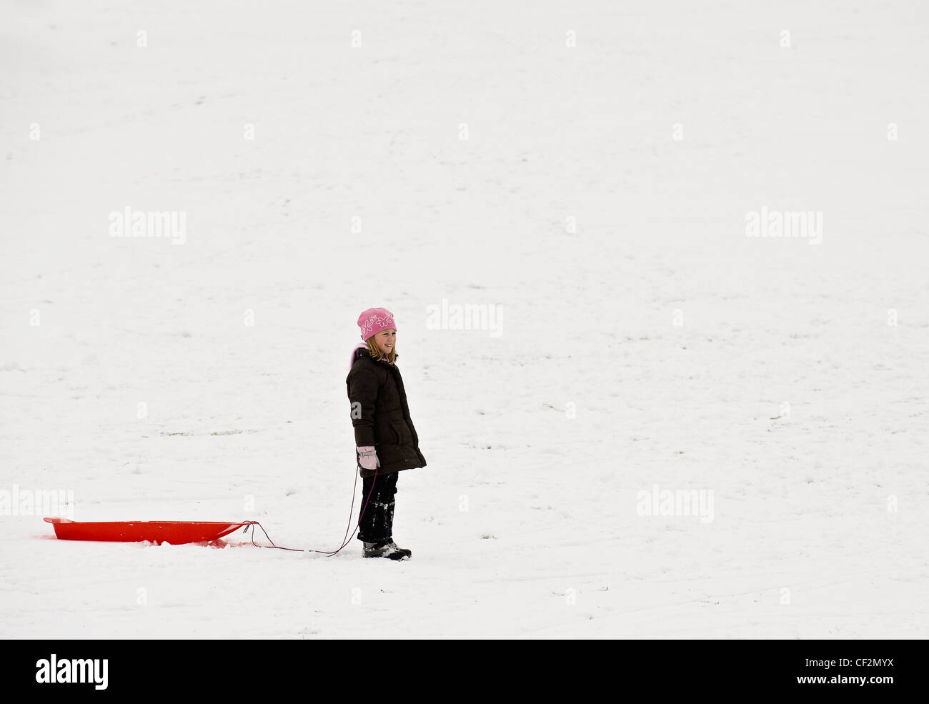 A young girl and her toboggan in the snow. Stock Photo