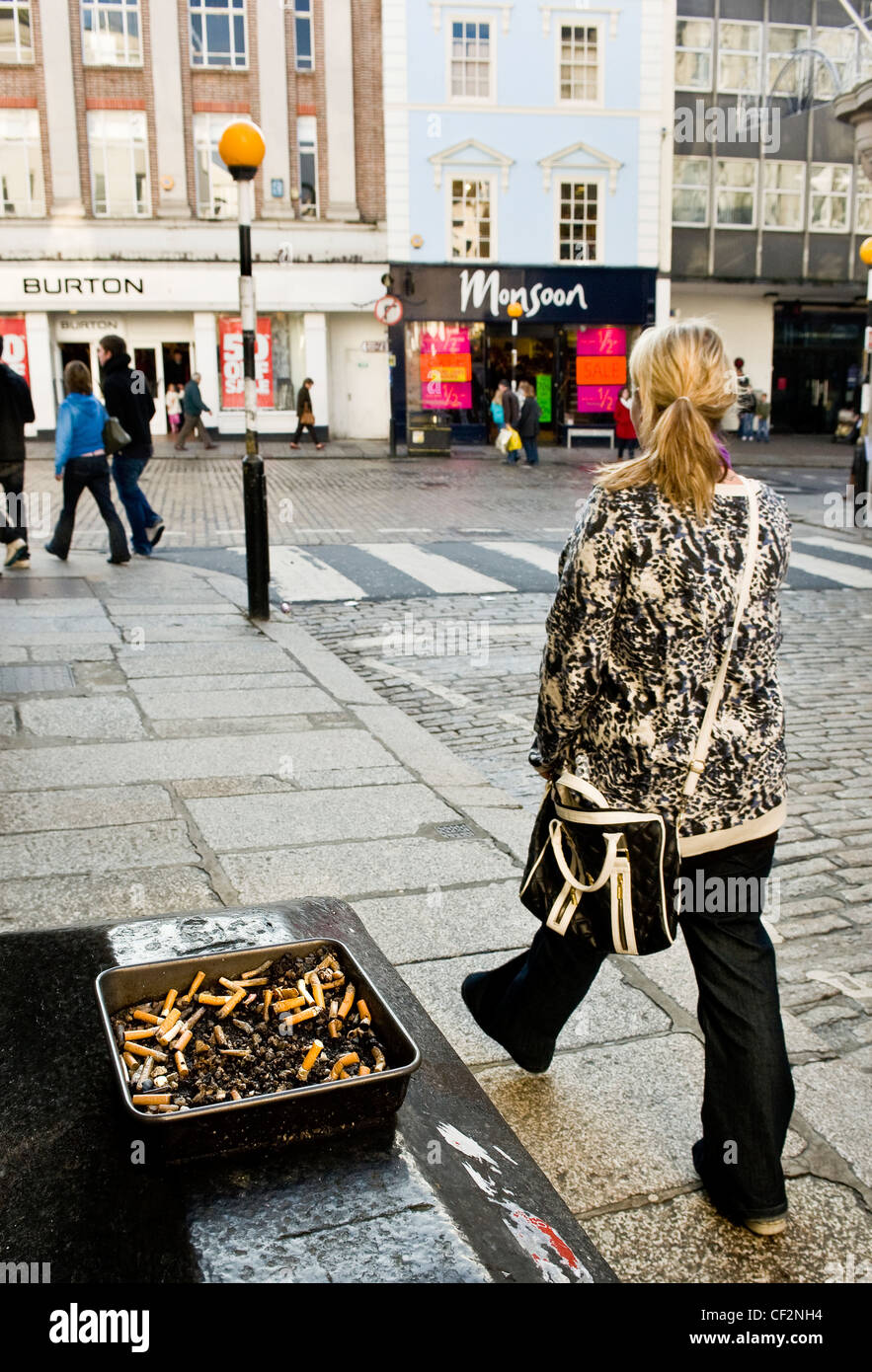 A woman walking past an ashtray full of cigarette butts in a street in Truro. Stock Photo