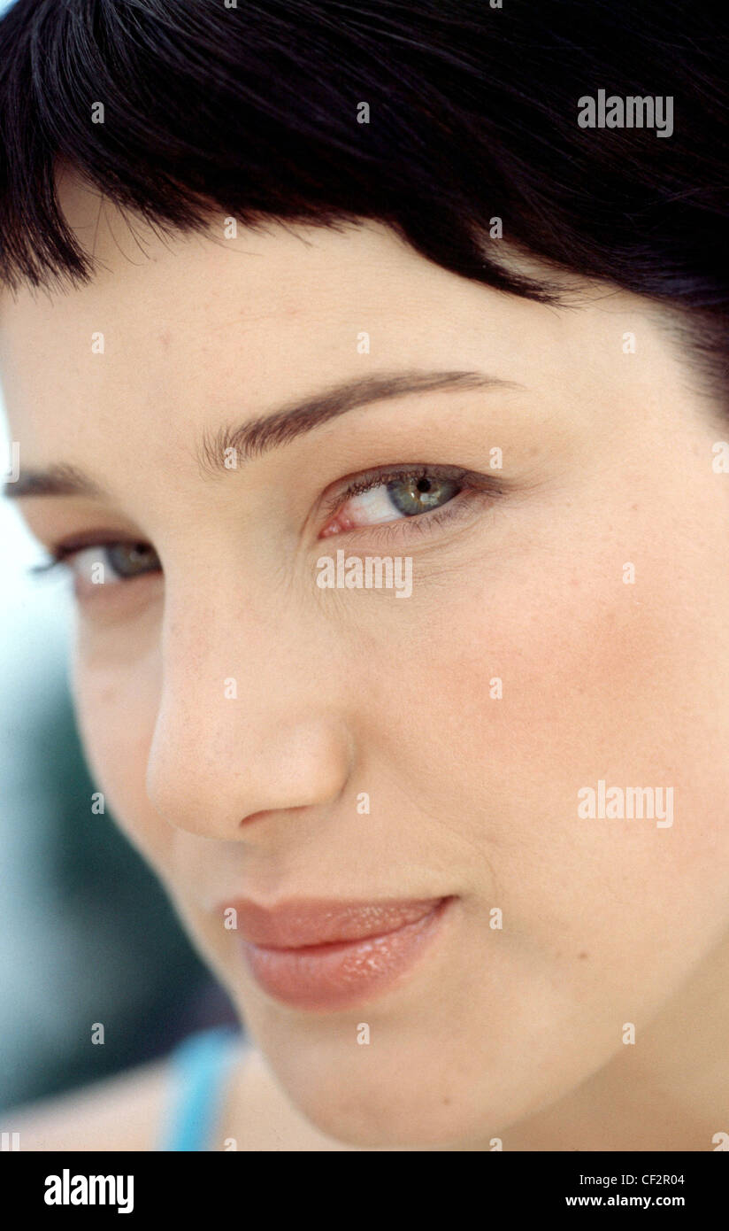 Semi profile of female black hair and short fringe wearing blue vest top lipgloss natural eye make up, looking to camera Stock Photo