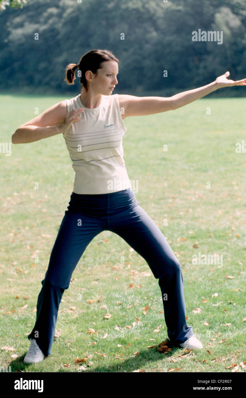 A Semi profile of female short auburn hair in ponytail wearing cream vest top navy blue tracksuit bottoms and trainers, doing Stock Photo