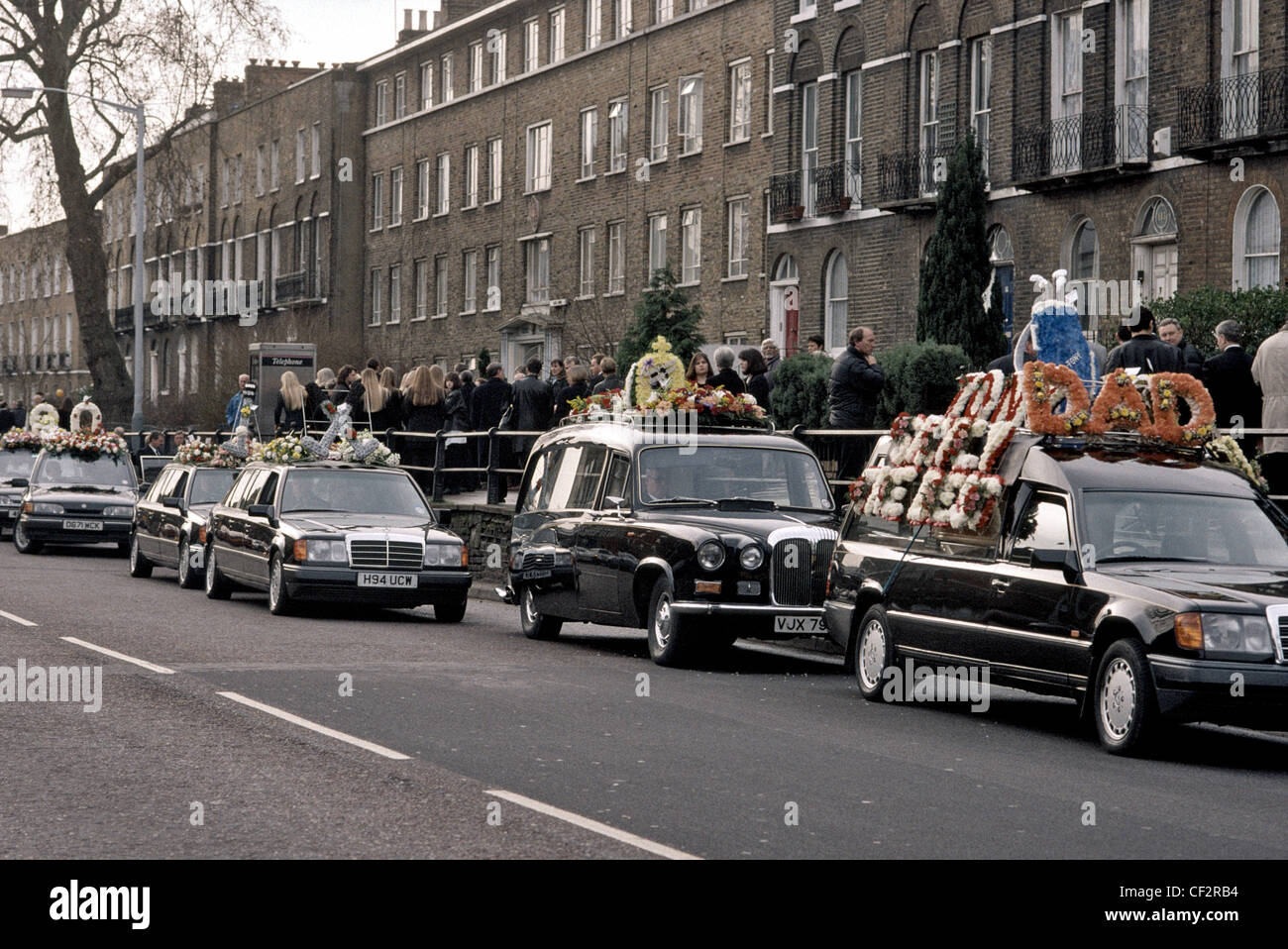 Procession of funeral cars laden with flowers on the roof follow the