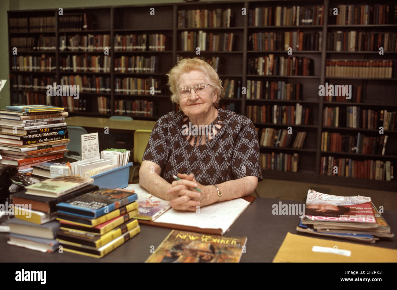 Old librarian looking to camera seated at check out desk in public ...
