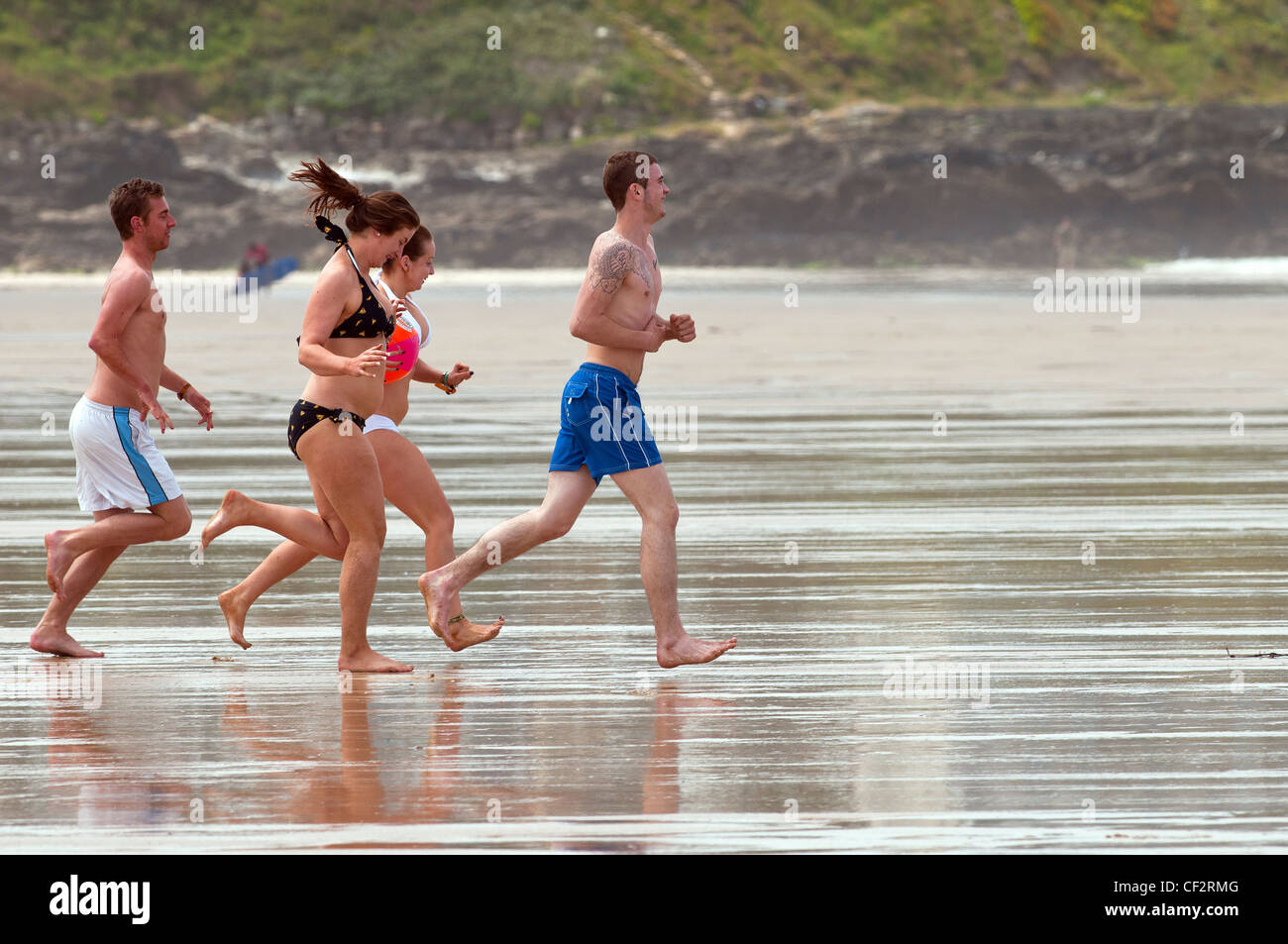People running across Fistral Beach towards the sea. Stock Photo