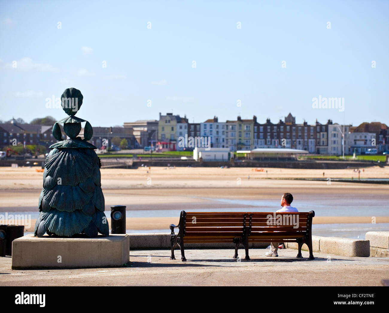 A man sitting on a bench on the Harbour Arm next to Mrs Booth, the Shell Lady of Margate, a 9 feet high bronze sculpture by Ann Stock Photo