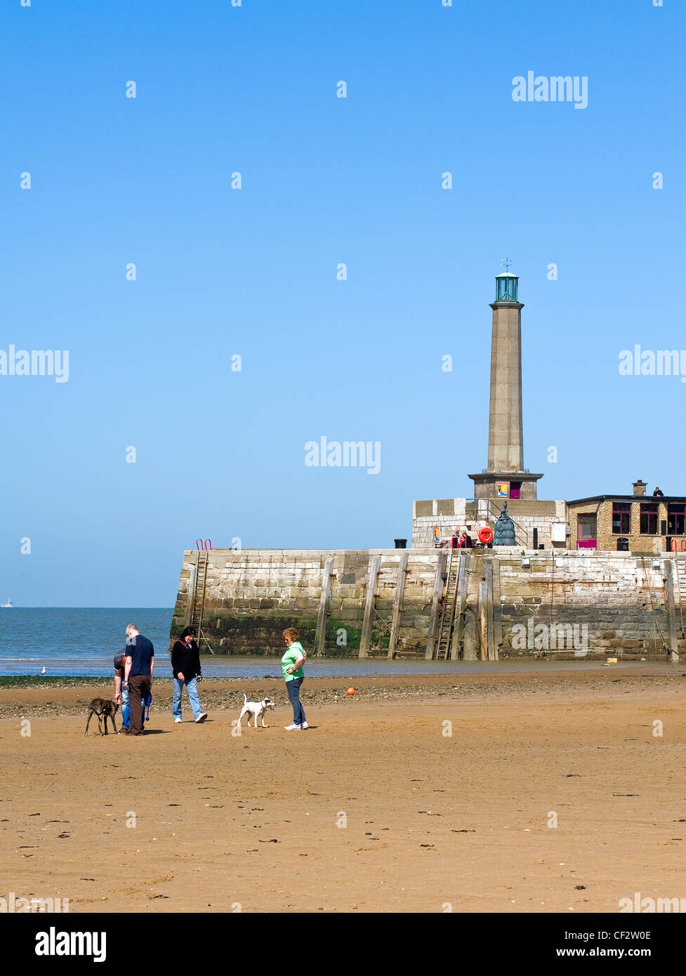 Dog walkers on the sandy beach at low tide with Margate lighthouse in the background. Stock Photo