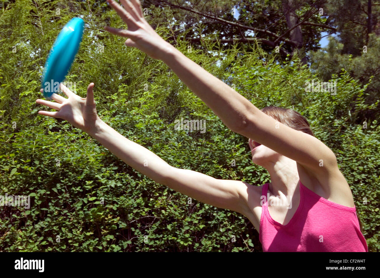 Female brunette hair off face wearing pink vest top arms raised to catch frisbee, arms partly obscuring face mouth open Stock Photo